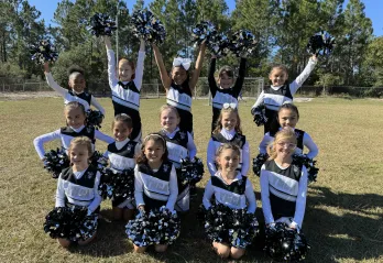 A youth cheer team takes a group photo together on the field at the Betty J. Pullum YMCA.
