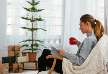 A woman is pictured enjoying a quiet moment in a living room decorated for Christmas, as she holds a mug in one hand and reads a book.