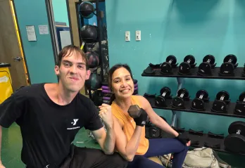 Josephine lifts weights and smiles for a photo, joined by staff member Andrew.