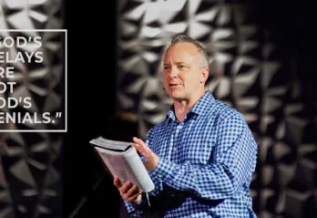 A pastor holds a Bible while speaking to a group.