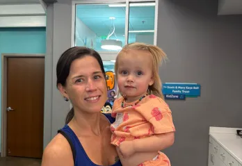 Bear Levin Studer YMCA member Ashley is pictured in the lobby of the branch with the KidZone visible behind her as she holds her daughter Breaia.