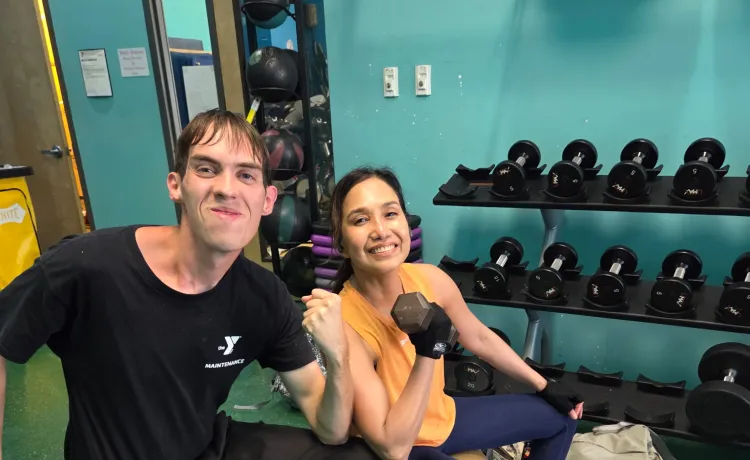 Josephine lifts weights and smiles for a photo, joined by staff member Andrew.
