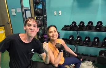 Josephine lifts weights and smiles for a photo, joined by staff member Andrew.