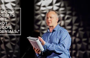 A pastor holds a Bible while speaking to a group.